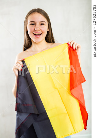 Reliant positive young woman holds big national flag of Belgium with confident smile Reliant positive young woman holds big national flag of Belgium with confident smile 127623782