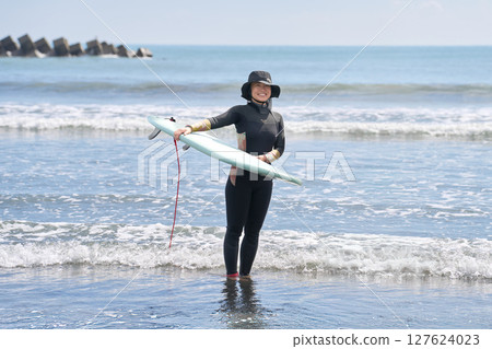 Female surfer standing in the ocean with her board 127624023