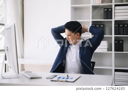 Overworked young Asian businessman office worker suffering from neck pain after had a long day at desk. office syndrome concept Overworked young Asian businessman office worker suffering from neck pain after had a long day at desk. office syndrome concept 127624285