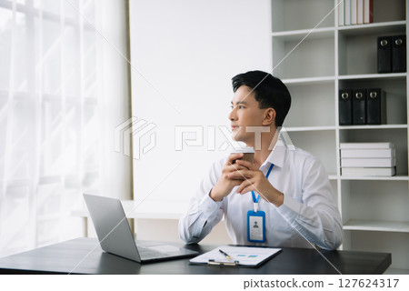 Young Asian business man using laptop and tablet while sitting at her working place. Concentrated at work. 127624317