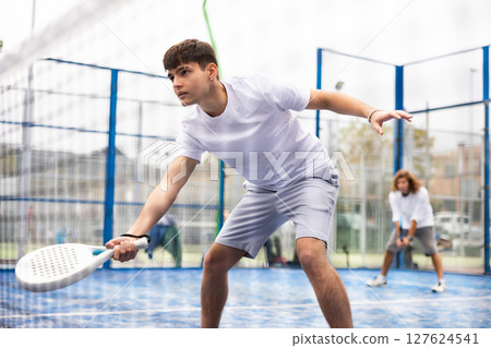 Male player ready to hits the ball while playing padel on hard court 127624541