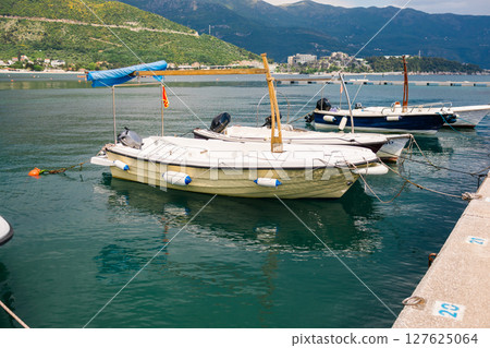 Small motorboats docked in calm marina water. Seaside lifestyle, coastal transportation, and nautical summer atmosphere Small motorboats docked in calm marina water. Seaside lifestyle, coastal transportation, and nautical summer atmosphere 127625064