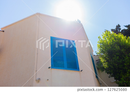 Blue shutter on beige wall. Mediterranean architecture, summer aesthetic, and coastal urban design with natural elements. Blue shutter on beige wall. Mediterranean architecture, summer aesthetic, and coastal urban design with natural elements. 127625080