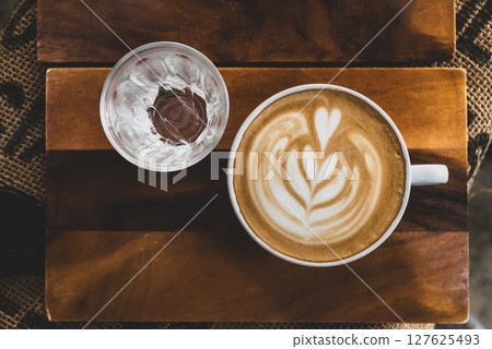Cup of latte art coffee and cold water on wooden plate, Table top view Cup of latte art coffee and cold water on wooden plate, Table top view 127625493