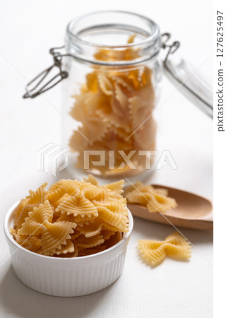 Raw farfalle pasta in a white bowl and glass jar on white background, Italian food ingredient 127625497