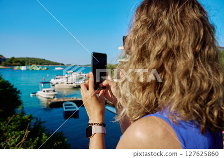 Woman taking photo with smartphone near sea 127625860