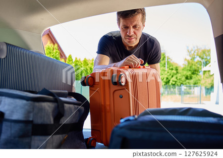 Man loading suitcase into car trunk before travel departure Man loading suitcase into car trunk before travel departure 127625924