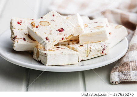 White nougat bars with almonds and dried fruit on plate on white table. White nougat bars with almonds and dried fruit on plate on white table. 127626270