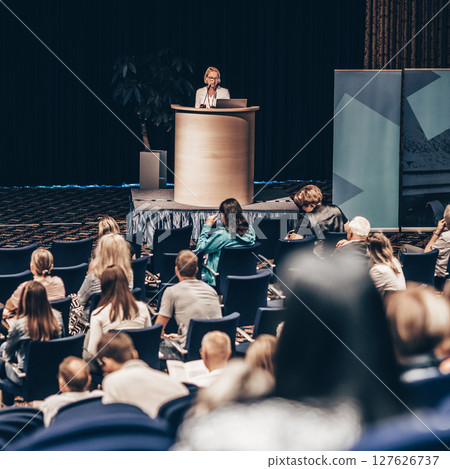 Female speaker giving a talk on corporate business conference. Unrecognizable people in audience at conference hall. Business and Entrepreneurship event 127626737