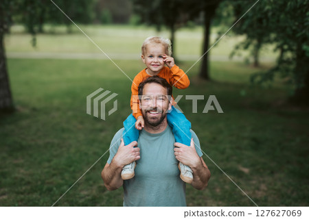 Father carrying his smiling son on shoulders during walk in park Father carrying his smiling son on shoulders during walk in park 127627069