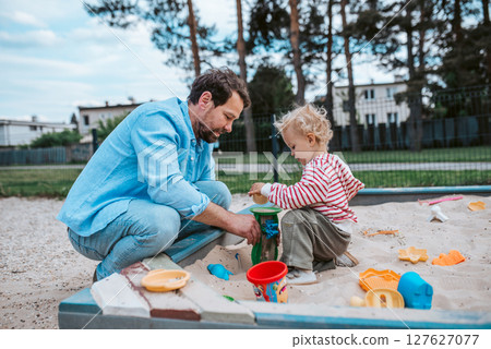 Father and little toddler son playing in the sandbox on playground. Father and little toddler son playing in the sandbox on playground. 127627077
