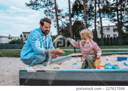 Father and little toddler son playing in the sandbox on playground. 127627086