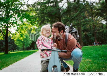 Toddler riding balance bike with dad cheering behind Toddler riding balance bike with dad cheering behind 127627089