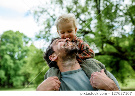 Father carrying his smiling son on shoulders during walk in park Father carrying his smiling son on shoulders during walk in park 127627107