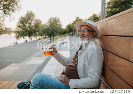 Senior man enjoying beer on sunny riverside promenade 127627119