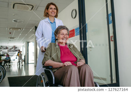 Geriatric doctor pushing a patient in a wheelchair down a hospital hallway. Geriatric doctor pushing a patient in a wheelchair down a hospital hallway. 127627164