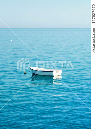 平靜無波的藍色水面,一艘孤獨的小船漂浮在上面 平靜無波的藍色水面,一艘孤獨的小船漂浮在上面 127627670