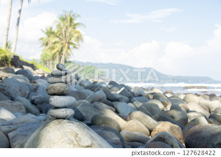 Zen Stone Balance on Rocky Beach with coconut trees on the shore and mountain backdrop 127628422