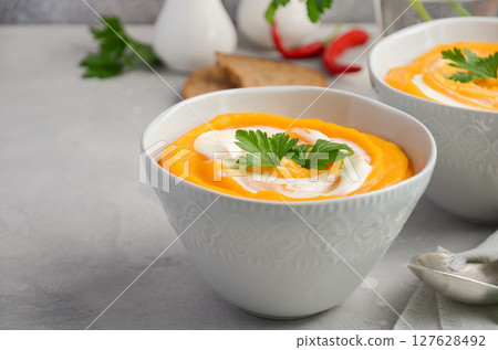 Pumpkin soup with cream and parsley on a grey concrete or stone background, selective focus Pumpkin soup with cream and parsley on a grey concrete or stone background, selective focus 127628492