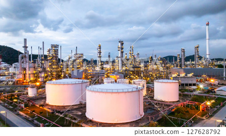 Oil refinery petrochemical plant at dusk illuminated storage tank industrial infrastructure, Oil refinery petrochemical product storage tank at oil refinery factory industry, Global energy refinery. 127628792