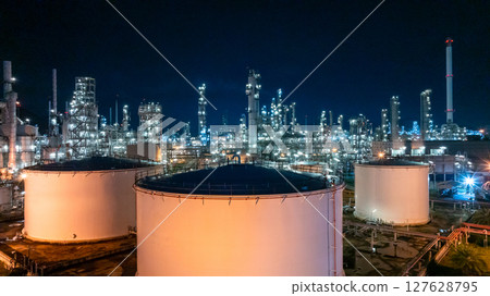 Oil refinery petrochemical plant at night illuminated storage tank industrial infrastructure, Oil refinery petrochemical product storage tank at oil refinery factory industry, Global energy refinery. 127628795