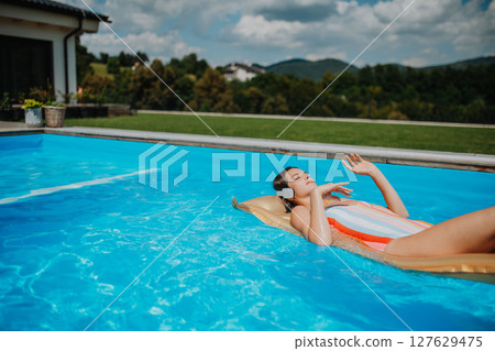 Top view of young woman in swimming pool outdoors on floating bed, relaxing. 127629475