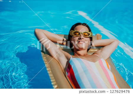 Top view of young woman in swimming pool outdoors on floating bed, relaxing. Top view of young woman in swimming pool outdoors on floating bed, relaxing. 127629476