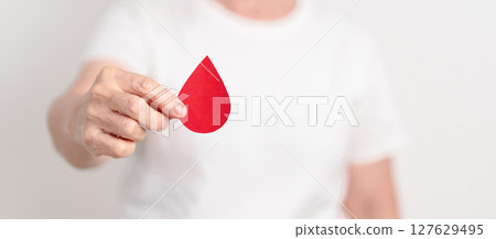 Elderly woman with red Blood drop paper for concept of June World Blood Donor day, Donation, April Hemophilia awareness day, May Thalassemia Day, Anemia awareness, June Sickle Cell and Blood Disorders 127629495