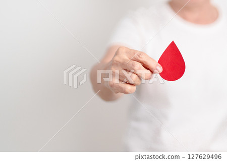 Elderly woman with red Blood drop paper for concept of June World Blood Donor day, Donation, April Hemophilia awareness day, May Thalassemia Day, Anemia awareness, June Sickle Cell and Blood Disorders 127629496