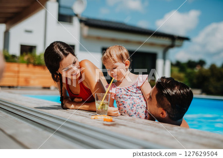 Young family with small daughter in swimming pool outdoors in backyard garden. 127629504