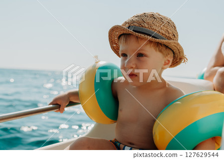 A small boy with arm floaties sitting on boat on summer holiday. A small boy with arm floaties sitting on boat on summer holiday. 127629544