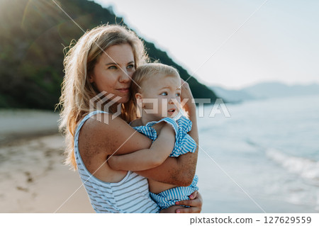 Tender moment between young mom and daughter on sunny beach vacation 127629559