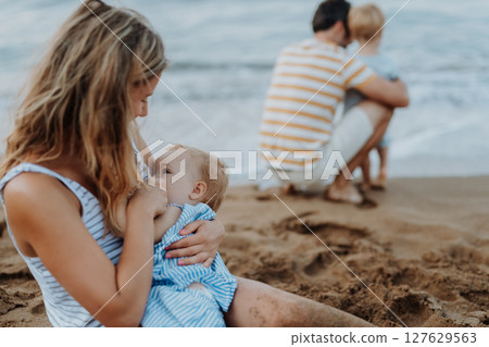 Young mother breasfeeding toddler daughter on beach on summer holiday. Young mother breasfeeding toddler daughter on beach on summer holiday. 127629563