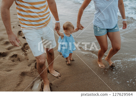 Parents holding hands with little toddler girl, walking on beach during beach holiday. Parents holding hands with little toddler girl, walking on beach during beach holiday. 127629564