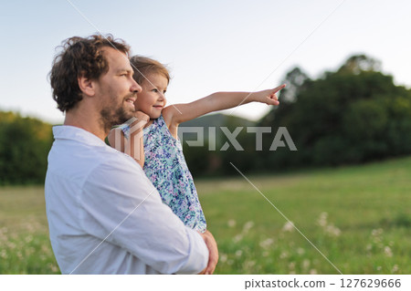 Father standing in the middle of meadow, holding small daughter in the arms. 127629666
