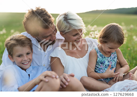 Young family with small children in summer nature at sunset, sitting in the grass. 127629668