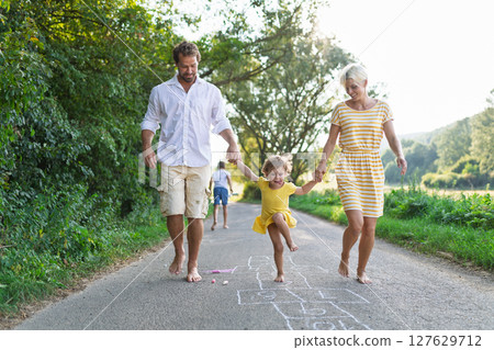 Parents helping litthe girl with hopscotch during warm summer day. 127629712