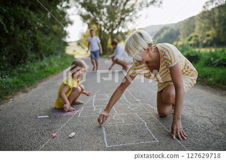 Mom and girl drawing with chalk on road. . 127629718