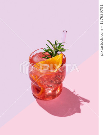 Red orange cocktail or lemonade with ice and rosemary on a pink background with shadows. Red orange cocktail or lemonade with ice and rosemary on a pink background with shadows. 127629791