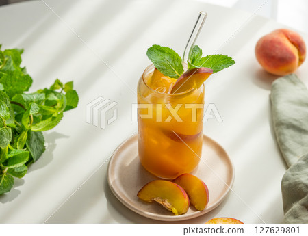 Peach drink or tea with ice, mint in a glass on a white table with fresh fruits, herbs, napkin Peach drink or tea with ice, mint in a glass on a white table with fresh fruits, herbs, napkin 127629801