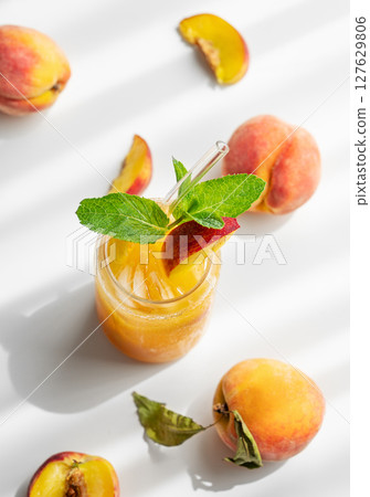 Peach drink or tea with ice, mint in a glass on a white table with fresh fruits and sunlight. 127629806