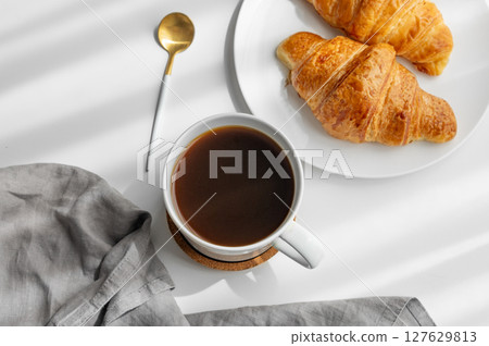 Coffee espresso cup and fresh croissants on a white background with morning shadows and napkin. 127629813