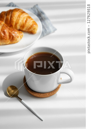 Coffee espresso cup and fresh croissants on a plate  on a white background with morning shadows. 127629818