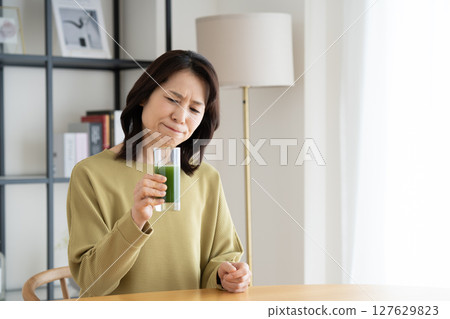 Middle-aged woman drinking green juice at home 127629823