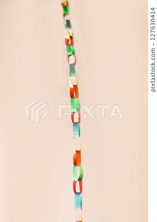 Vertical chain of interlinked colorful paper rings suspended against soft beige background. This vibrant handmade garland , childhood creativity, festive decor, crafting with simple materials Vertical chain of interlinked colorful paper rings suspended against soft beige background. This vibrant handmade garland , childhood creativity, festive decor, crafting with simple materials 127630414
