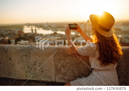 Young Woman on vacation using mobile phone to take photo of sunset of city. Rest, lifestyle concept. Young Woman on vacation using mobile phone to take photo of sunset of city. Rest, lifestyle concept. 127630878