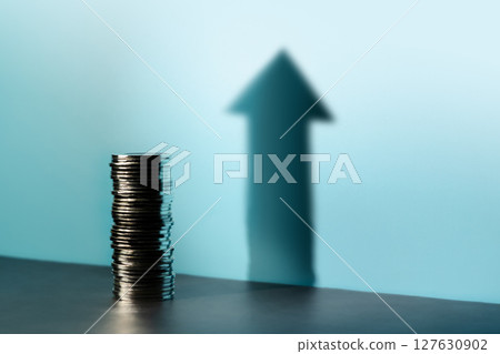 Coins stacked cast a tall upward arrow shadow, reflecting financial growth, investment optimism, and a hopeful economic outlook 127630902