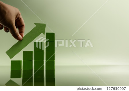 Hand placing green arrow on stacked bars, representing financial growth, rising profits, successful investment, and business recovery 127630907