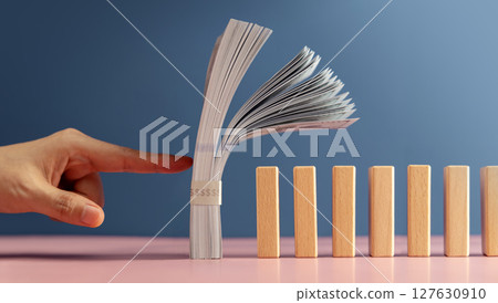 A finger about to push US dollar stack onto dominos, symbolizing economic risk, global financial instability, and the impact of powerful nations like the USA 127630910