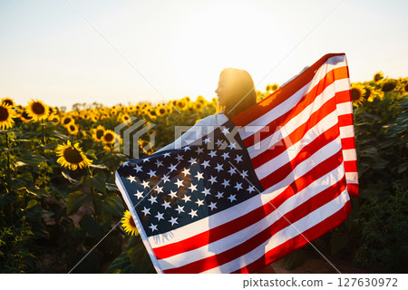 Woman proudly hold waving american USA flag in in the sunflower field. Independence Day, 4th July. 127630972